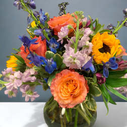 Colorful bouquet of roses, sunflowers, and blue flowers in a glass vase
