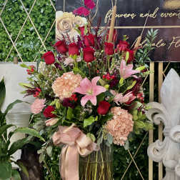Tall bouquet of red roses and pink lilies in a glass vase with a ribbon