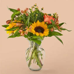 Sunflowers and peach roses arranged in a clear glass vase