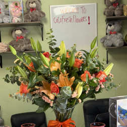 Orange lilies and roses in a glass vase with an orange ribbon