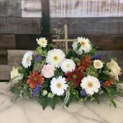 Low floral arrangement with white, orange, and pale pink blooms in a rope-wrapped cross base