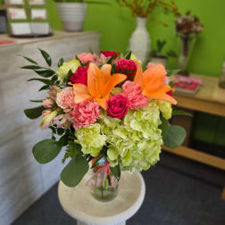 Bouquet of orange lilies, pink roses, and green hydrangeas in a glass vase