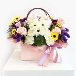 Pink and white floral arrangement in a gift box with a teddy bear face