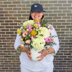 Person holding a colorful flower arrangement in a white vase