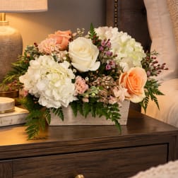 Cream and peach floral arrangement in a white wooden box on a bedside table