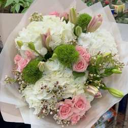 Bouquet of pink roses, white hydrangeas, and green pom-pom flowers wrapped in pale paper.