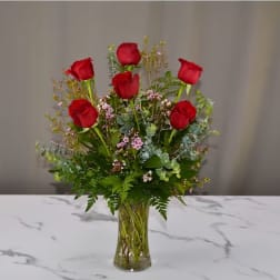 Red roses arranged in a clear glass vase with mixed greenery