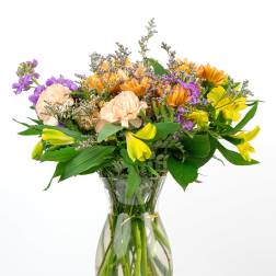 Mixed bouquet of yellow, purple, and peach flowers in a clear glass vase