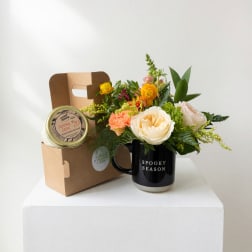 Flower arrangement in a black mug with a candle gift box beside it
