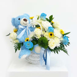 Blue teddy bear in a white basket with white and blue flowers
