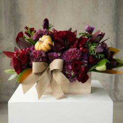 Red and purple floral arrangement in a wooden box with a burlap bow