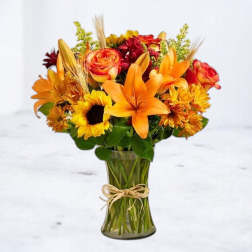 Orange lilies, roses, and sunflowers in a glass vase with a twine bow