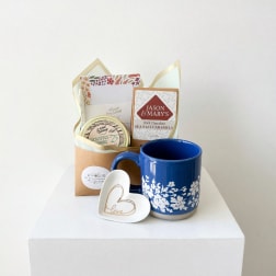 Gift basket with a blue floral mug, heart dish, candle, and chocolates