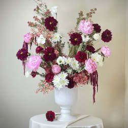 Tall arrangement of burgundy, pink, and white flowers in a white urn on a draped round table