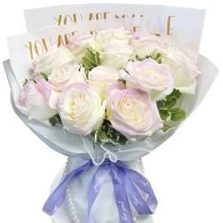 Bouquet of pale pink and white roses wrapped in white paper with a purple ribbon