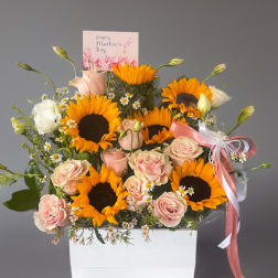 Pink roses and sunflowers arranged in a white box with a Mother's Day card