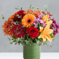 Mixed bouquet of orange, red, and purple flowers in a green vase