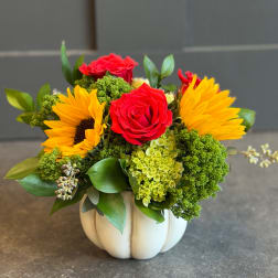 Red roses and yellow sunflowers in a white pumpkin vase