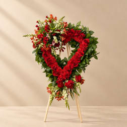 Heart-shaped floral wreath of red roses and mixed blooms on a wooden stand