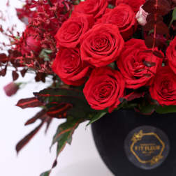 Red roses arranged in a black vase with dark foliage