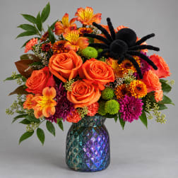 Orange and purple mixed bouquet in a faceted glass vase with a black spider decoration