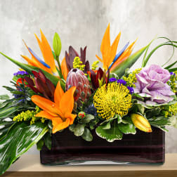 Tropical floral arrangement with orange and purple blooms in a rectangular vase