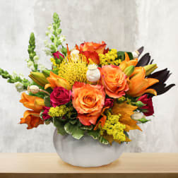 Orange and red mixed bouquet in a round white vase