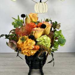 Halloween floral arrangement in a black skull vase with pumpkins