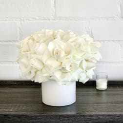 White rose bouquet in a white vase beside a small candle