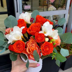 Compact orange and white rose arrangement in a white pot held outside a flower shop
