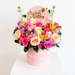 Pink and peach rose arrangement in a round box with a birthday sign