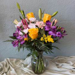 Mixed bouquet of yellow roses, purple alstroemeria, lilies, and daisies in a glass vase