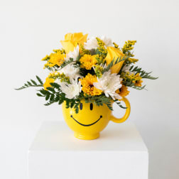 Yellow and white flower arrangement in a smiley-face mug