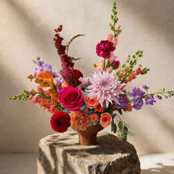 Colorful mixed flower arrangement in a brown vase on a stone pedestal