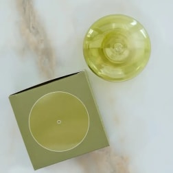 Green box and a yellow glass candle holder on a light surface