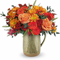 Orange and red flower arrangement in a ceramic pitcher vase