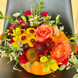 Fall floral arrangement in an orange pumpkin container with roses and mums