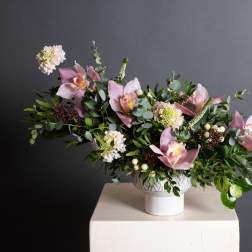 Pink orchid arrangement in a white pedestal vase