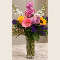 Mixed bouquet of pink, yellow, white, and purple flowers in a clear glass vase