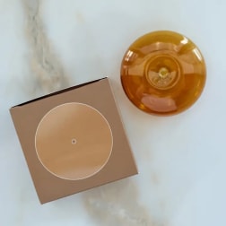 Amber glass candle and a tan square box on a light surface
