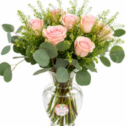 Pink roses arranged in a clear glass vase with eucalyptus foliage