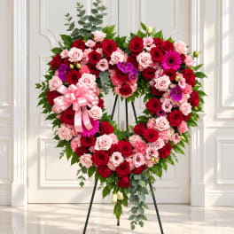Heart-shaped floral wreath with red and pink roses and a pink ribbon bow