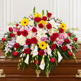 Large floral spray on a casket with red roses, white lilies, and yellow daisies
