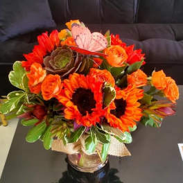 Bright orange sunflower and rose arrangement with succulent in a glass vase