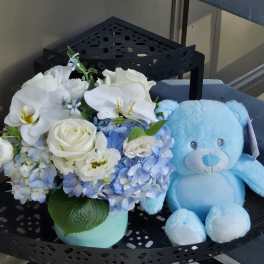 White and blue flower arrangement beside a light blue teddy bear