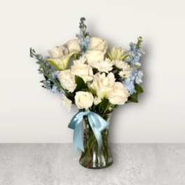 White flowers and pale blue blooms in a glass vase with a blue ribbon