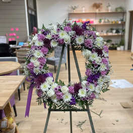 Purple and white floral wreath on an easel with a ribbon