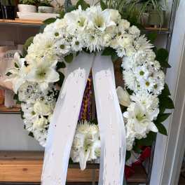 White funeral wreath with lilies, roses, and daisies on a stand