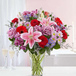 Mixed bouquet of roses, lilies, and daisies in a clear glass vase