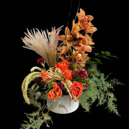 Orange roses and orchids in a white vase with dried grasses